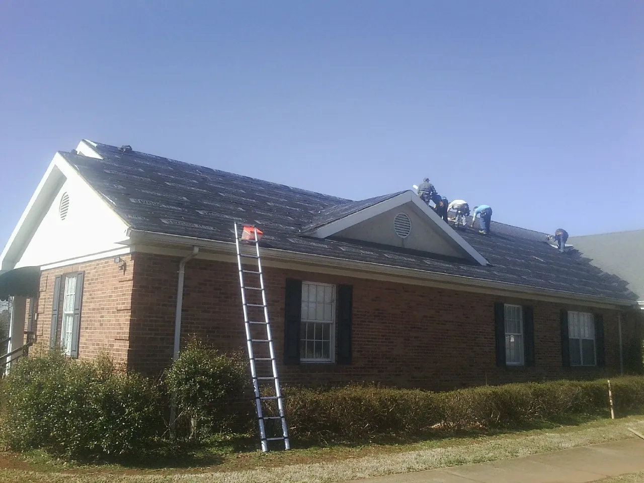 Crew tearing shingles off a brick ranch roof with a ladder set — Emergency Roof Repair work by our crew in Port Deposit