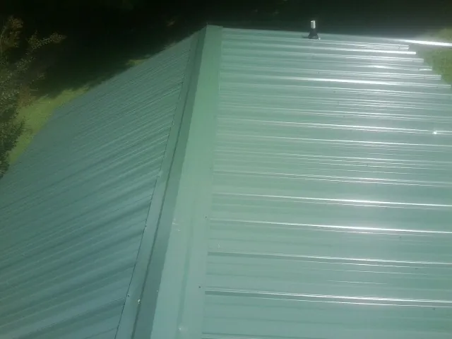 New green metal panels meeting at the ridge of a roof — Flat Roof Repair work by our crew in Port Deposit
