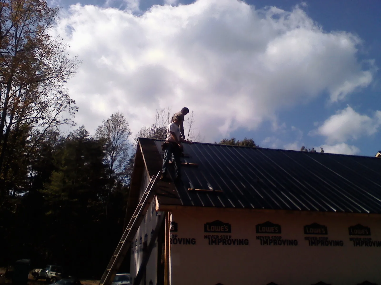 Roofer fastening dark metal panels high against a cloudy sky, from a Roof Inspection job in Port Deposit