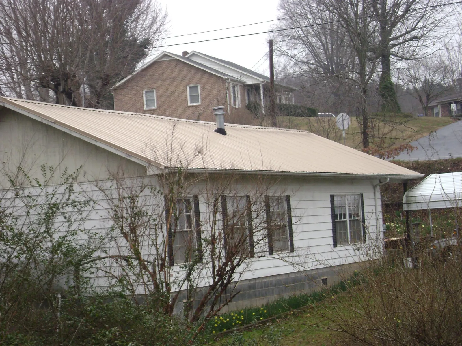 Tan metal roof on a white sided house set into a hillside — Commercial Roofing by Roofing Brothers in Port Deposit